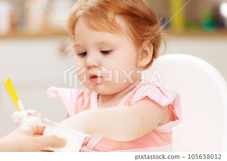 A baby eating yogurt with some on her face. A baby eating yogurt with some on her face. 105638012