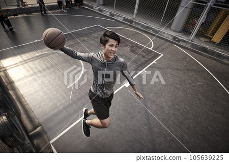 young asian adult male basketball player attempting a slam dunk on outdoor court 105639225