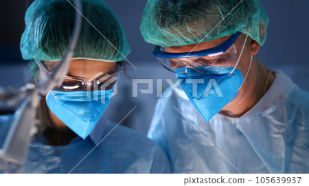 Close-up of serious professional surgeons in blue masks at operating room. 105639937