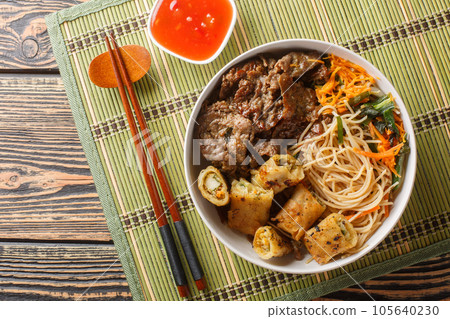 Bun Bo Xao is a Vietnamese noodle salad made with marinated flank steak, vermicelli noodles, vegetables and crispy nem spring rolls closeup. Horizontal top view Bun Bo Xao is a Vietnamese noodle salad made with marinated flank steak, vermicelli noodles, vegetables and crispy nem spring rolls closeup. Horizontal top view 105640230