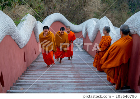 Senior monks stand and look to young monks during they walk on stair of the temple up to church Senior monks stand and look to young monks during they walk on stair of the temple up to church 105640790