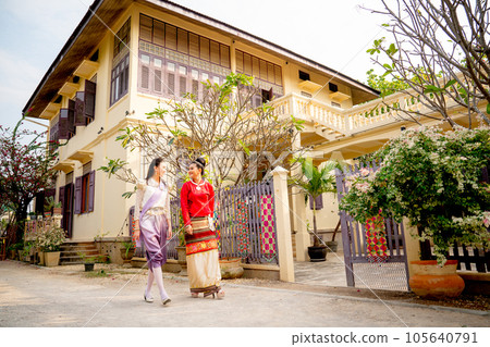 Wide shot of two young Asian women walk together in front of public ancient house in Thailand Wide shot of two young Asian women walk together in front of public ancient house in Thailand 105640791