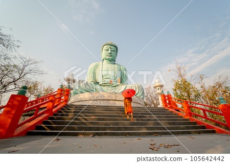 Wide shot side view back of young Asian monk hold red umbrella and walk up on stair in front statue Wide shot side view back of young Asian monk hold red umbrella and walk up on stair in front statue 105642442
