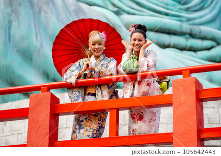 Two Asian pretty women stay close to red railing in the area of base of green big buddha statu 105642443