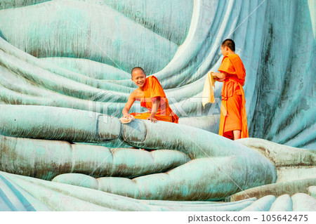 Two young Asian monk stay with other monk on green big buddha statue to clean in area of body statue Two young Asian monk stay with other monk on green big buddha statue to clean in area of body statue 105642475