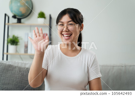 Portrait of young Asian woman wearing eye glasses big smiling and looking at camera with feeling happy and positive in living room at home, meeting, video conference. Portrait of young Asian woman wearing eye glasses big smiling and looking at camera with feeling happy and positive in living room at home, meeting, video conference. 105642493