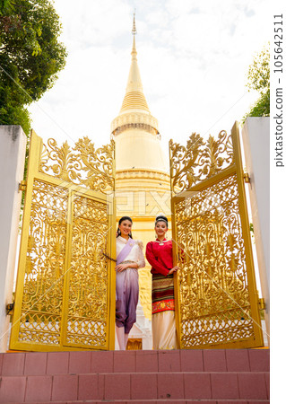 Vertical image of two women stand in front of golden gate of the temple and pagoda in the back 105642511