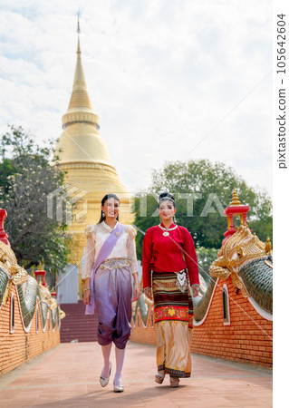 Vertical image of Thai women with traditional dress walk together and discuss on walkway of temple Vertical image of Thai women with traditional dress walk together and discuss on walkway of temple 105642604