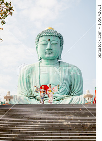 Two Asian young woman with japanese style dress stay on base of green big buddha statue 105642611