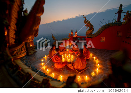 Side view of young and senior monk sit in a circle with several lighting candle around in temple 105642614
