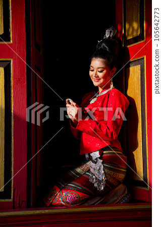 Vertical image of lovely Asian Thai woman wear Thai Lanna traditional style sit at the red door 105642773