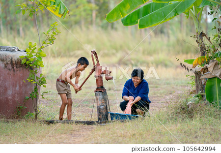 Asian boy help her mother or senior woman to wash pink cloth using underground water 105642994