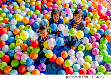 Group of three Asian girls sit among many paper lamps with multicolor and they look happy Group of three Asian girls sit among many paper lamps with multicolor and they look happy 105643208