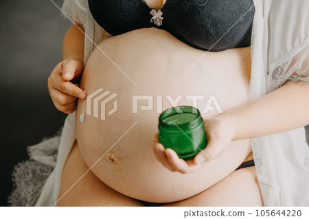 Young pregnant woman with the belly smearing cream against stretch marks, pregnancy concept 105644220