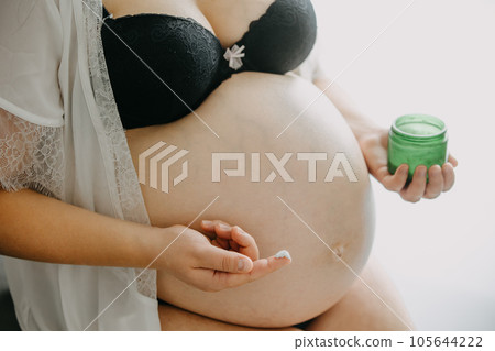 Young pregnant woman with the belly smearing cream against stretch marks, pregnancy concept 105644222