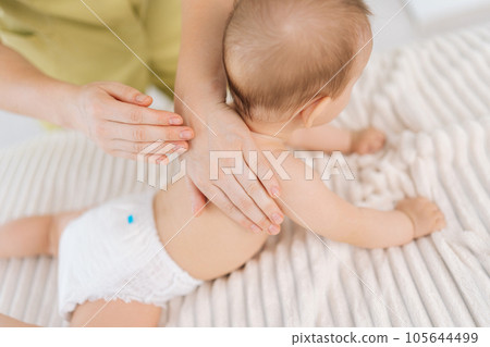 Closeup top view of loving mother hands massaging little baby. Close up cropped shot of unrecognizable masseuse female hands doing massage to newborn. Back view of cute infant baby lying on stomach. Closeup top view of loving mother hands massaging little baby. Close up cropped shot of unrecognizable masseuse female hands doing massage to newborn. Back view of cute infant baby lying on stomach. 105644499