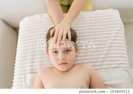 Closeup top view of cute five year old boy laying on bed at manual therapist in osteopath cabinet receiving manual therapy. Professional female physiotherapist adjustment neck, holding head. 105644512