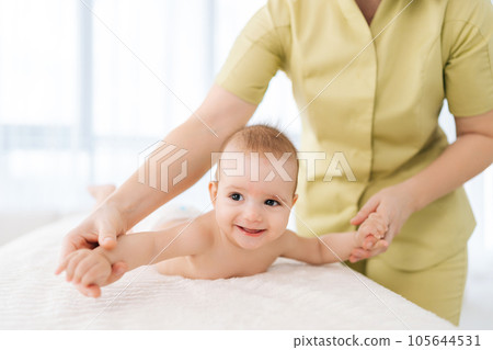 Cropped shot of unrecognizable pediatric masseur with cute baby boy doing exercise simple exercises to make baby bones and muscles stronger. Portrait of laughing newborn infant lying on bed. 105644531