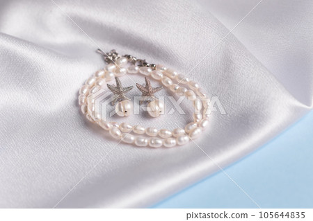 Elegance pearl bracelet and earring on silk fabric background. Jewellery and handmade accessories concept Elegance pearl bracelet and earring on silk fabric background. Jewellery and handmade accessories concept 105644835