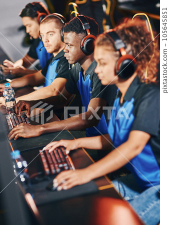 Professional cybersport team wearing headphones participating in eSport tournament, playing online video games while sitting in gaming club or internet cafe Professional cybersport team wearing headphones participating in eSport tournament, playing online video games while sitting in gaming club or internet cafe 105645851