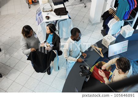 Shopping center cashier packing apparel and accepting payment while customers waiting at checkout desk top view. Diverse people buying clothes in boutique and standing in line at cash register 105646891