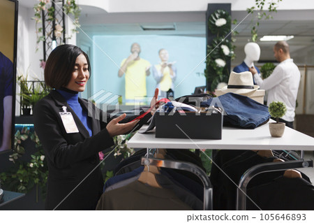 Clothing store smiling asian seller looking at stylish red tie while adjusting accessory on shelf. Department center boutique woman assistant managing merchandise in stock 105646893