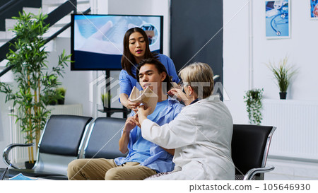 Elderly doctor helping patient to take of cervical neck collar in hospital waiting area, explaining health care treatment. Traumatologist receiving medicine support during checkup visit appointment 105646930