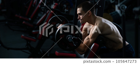 Man doing EZ barbell bicep exercises on Scott bench.  105647273