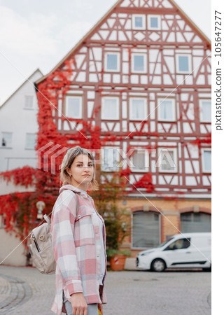 a beautiful girl stands against the background of the window of an old European house, entwined with a floating red color in autumn. Tourism & Travel Concept. Nice portrait of a young woman, in boho 105647277
