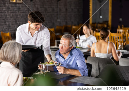 Young waiter serving salads to elderly couple in restaurant Young waiter serving salads to elderly couple in restaurant 105648329