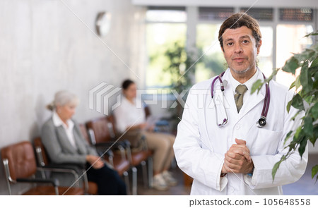 Smiling doctor in white lab coat standing in medical office Smiling doctor in white lab coat standing in medical office 105648558