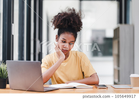 Young African American woman is taking notes in a notebook while watching a webinar video course. Afro american student listening to the lecture to study online through e-learning. Young African American woman is taking notes in a notebook while watching a webinar video course. Afro american student listening to the lecture to study online through e-learning. 105649917
