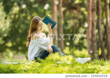 a beautiful young woman reading a book in the park 105650529