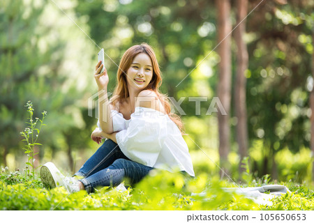 A beautiful young woman looking at her smartphone in the park A beautiful young woman looking at her smartphone in the park 105650653