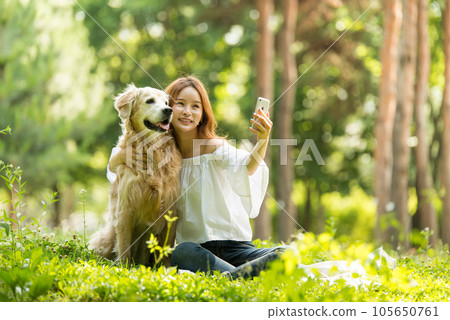 A beautiful young woman taking pictures with her dog on her smartphone in the park 105650761