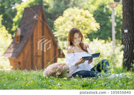 A beautiful young woman reading a book with her dog in the park A beautiful young woman reading a book with her dog in the park 105650840