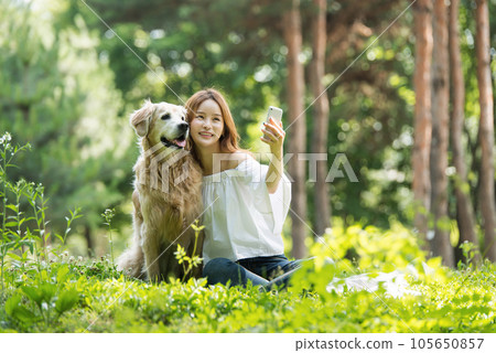 A beautiful young woman taking pictures with her dog on her smartphone in the park 105650857