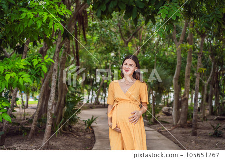 A serene and radiant pregnant woman after 40, surrounded by nature's beauty in the park, cherishing the journey of motherhood with a glowing smile 105651267
