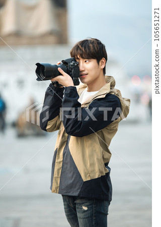 A young man holding a camera and taking pictures during a trip to Korea	 105651271