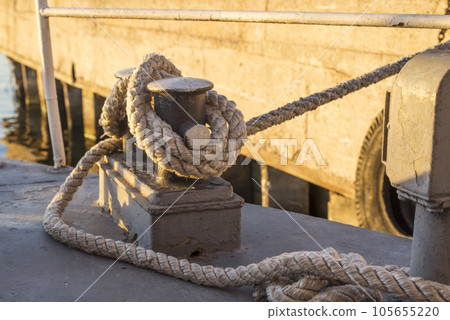 Tied rope knot on metallic bollard seafaring port. Nautical ship moored in dock Tied rope knot on metallic bollard seafaring port. Nautical ship moored in dock 105655220