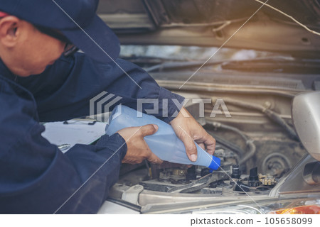 Car Mechanic man hands pouring Deionized purified Distilled water for car battery mechanical service. Close up hands man hold Deionized Distilled liquid water bottle at garage auto mobile car service 105658099