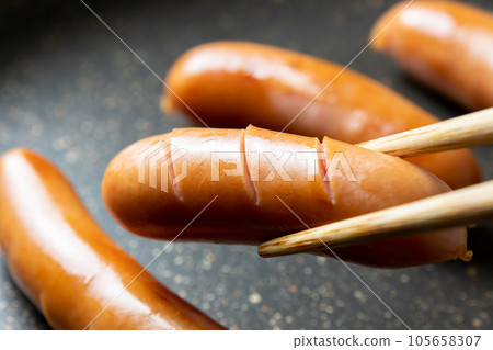 A cooking scene in which the wiener sausage is cut in and baked in a frying pan. 105658307