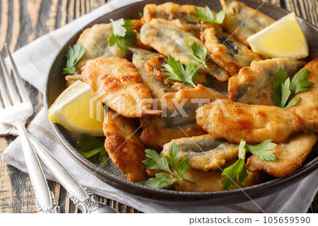 Fried breaded anchovy fillets served with lemon and herbs close-up on a plate. Horizontal 105659590