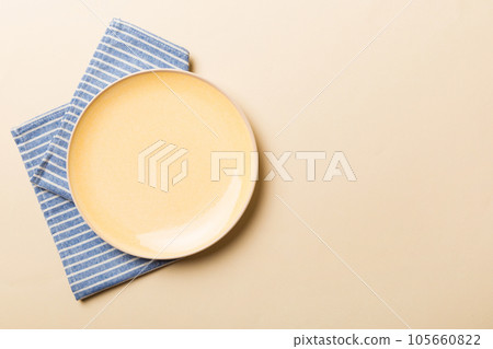 Top view on colored background empty round yellow plate on tablecloth for food. Empty dish on napkin with space for your design 105660822