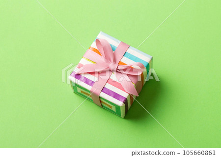 wrapped Christmas or other holiday handmade gift box in color paper with ribbon on colored background. Present box, decoration of gift on colored table, top view with copy space 105660861