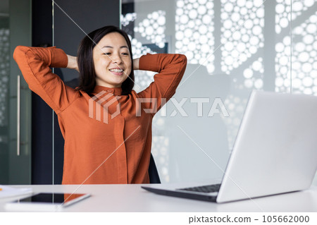Young Asian woman resting in the office, successfully completed the work, satisfied with the results of the achievement, put her hands behind her head, dreaming, looking at the laptop screen. Young Asian woman resting in the office, successfully completed the work, satisfied with the results of the achievement, put her hands behind her head, dreaming, looking at the laptop screen. 105662000