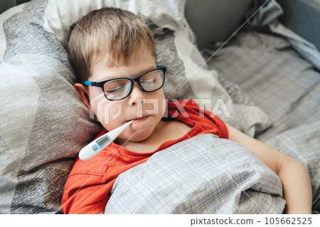 A boy with glasses lies on a bed with a thermometer in his mouth. Temperature measurement during a cold A boy with glasses lies on a bed with a thermometer in his mouth. Temperature measurement during a cold 105662525