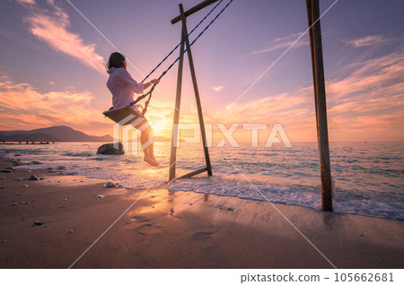Happy young woman on wooden swing in water, sea with waves 105662681