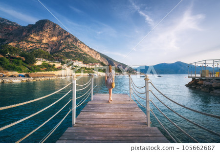 Young woman on wooden pier on sea shore is looking on mountain Young woman on wooden pier on sea shore is looking on mountain 105662687