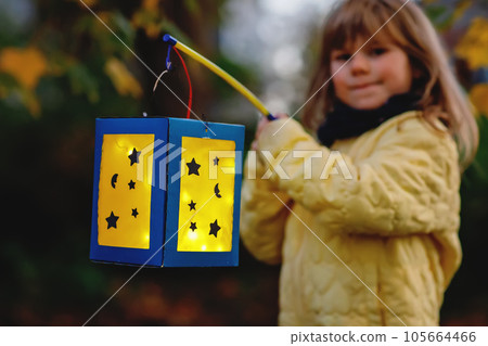 Closeup of little preschool kid girl holding selfmade traditional lanterns with candle for St. Martin procession. child happy about family parade in kindergarten. German tradition Martinsumzug Closeup of little preschool kid girl holding selfmade traditional lanterns with candle for St. Martin procession. child happy about family parade in kindergarten. German tradition Martinsumzug 105664466